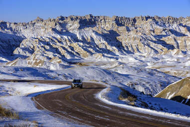 truck driving along road lined with snow covered badlands 